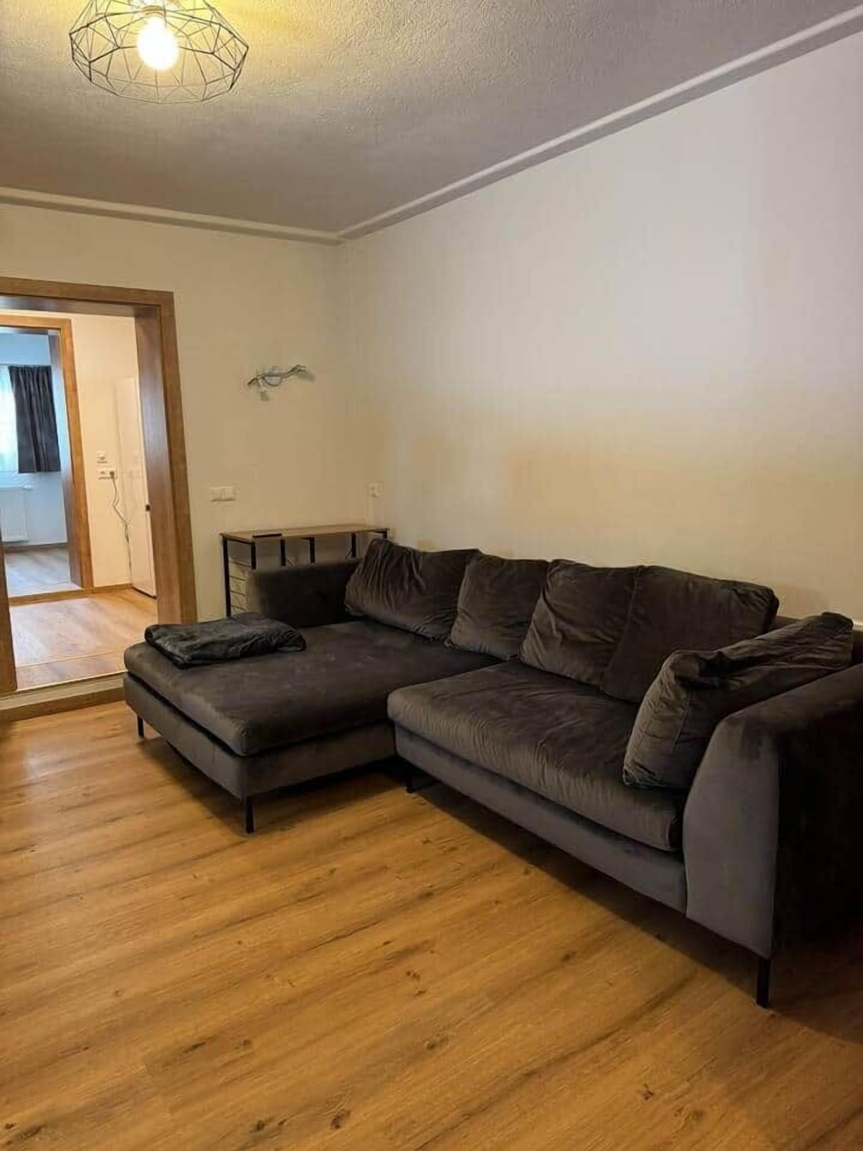 A living room with a sectional sofa, wooden flooring, and a geometric light fixture.