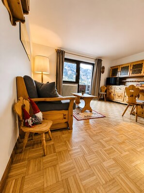 Ein gemütliches Wohnzimmer mit einer Couch, einem Holztisch und einer Küchenzeile mit Schränken und einem Fernseher.