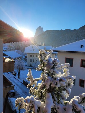 Paesaggio innevato con un edificio, alberi e montagne sullo sfondo.