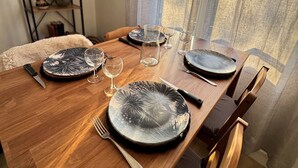 A dining table set with plates, glasses, and cutlery, with a window and curtains in the background.