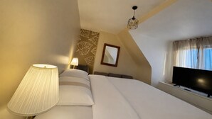 A hotel room with a bed, a bedside lamp, a flat-screen TV, a window with curtains, and a geometric wall pattern.