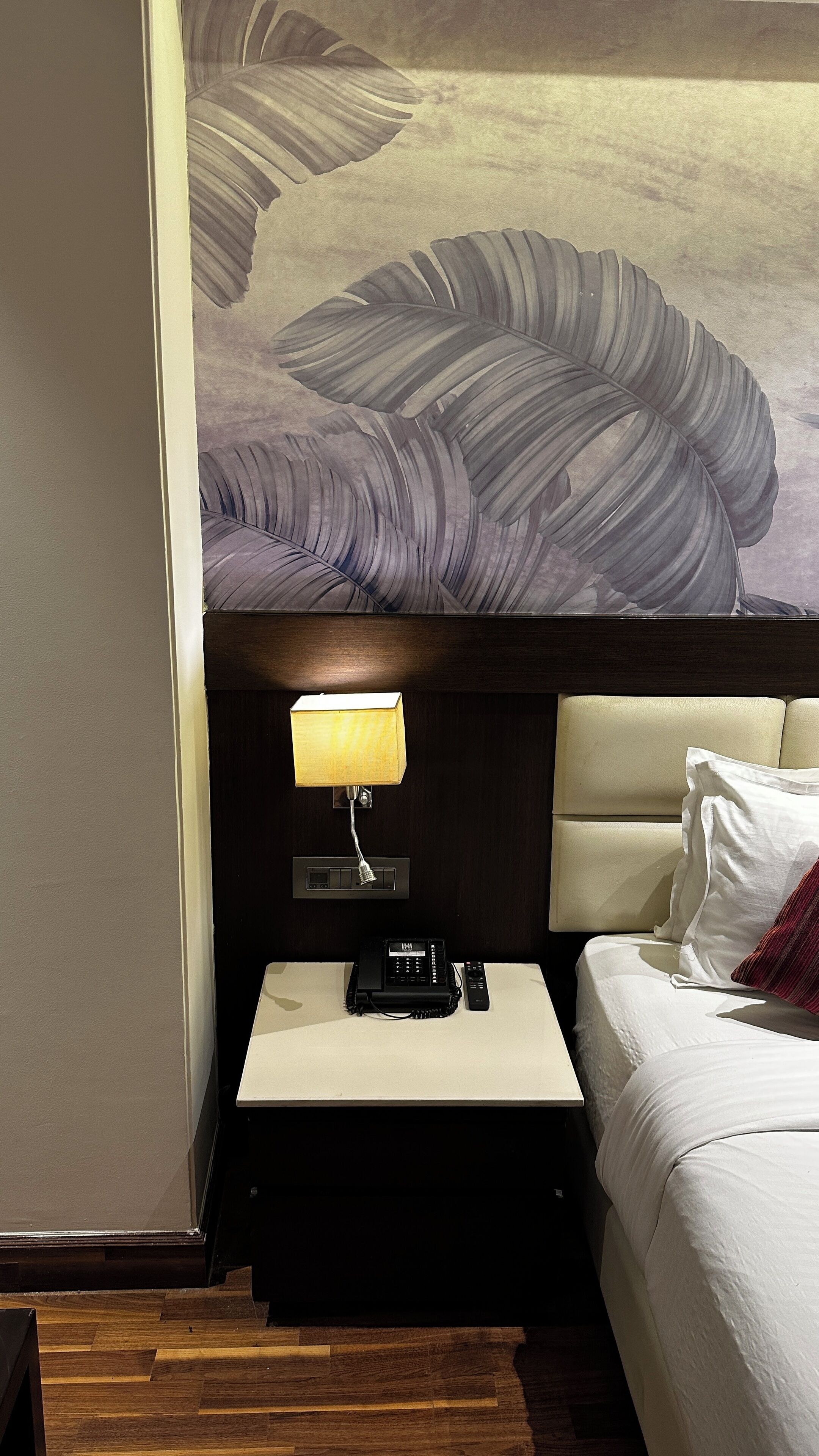 Una habitación de hotel con una cama, una mesita de noche con lámpara, un teléfono y un panel de control en la pared.