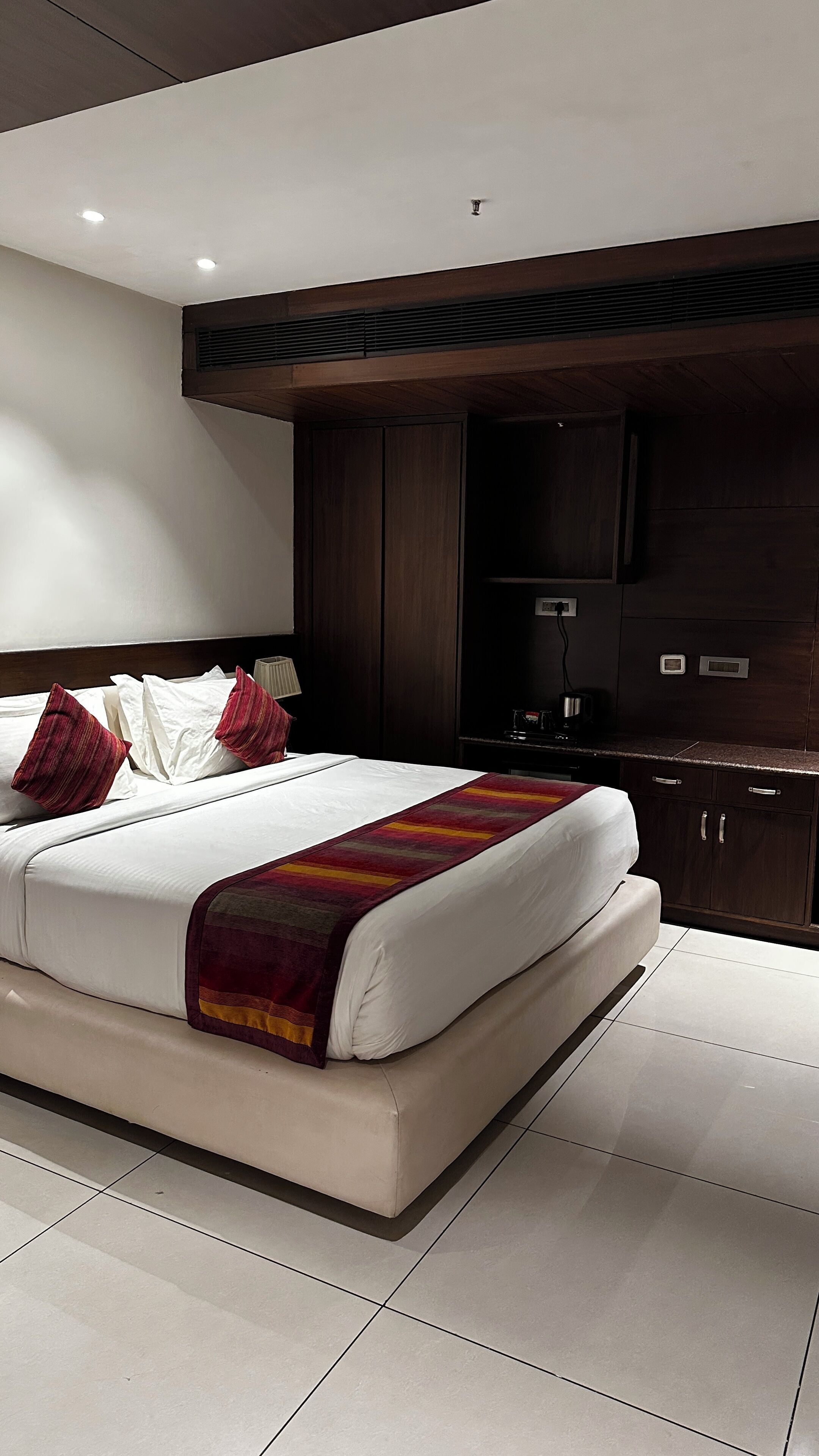 A modern hotel room with a large bed, dark wood cabinets, and a small kitchenette.