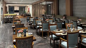 Un vaste espace dédié à la salle à manger, avec de nombreuses tables et chaises, un comptoir d’accueil et un design moderne du plafond agrémenté d’un éclairage encastré.