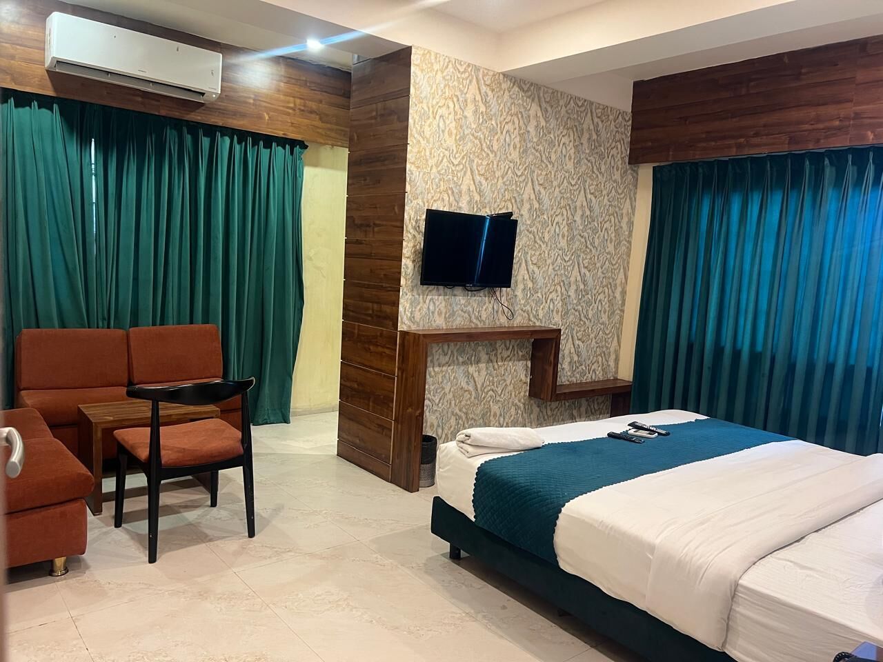 Een hotelkamer met een bed, een bank, een stoel, een televisie en een houten accentmuur.