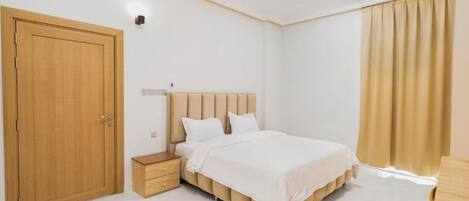 Un dormitorio con cama, mesita de noche, armario y cortinas.