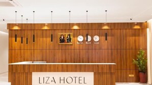 Ein Empfangsschalter mit Holzpaneelen, Uhren, die die Zeit in New York, Maskat und London anzeigen, und ein Schild mit der Aufschrift 'LIZA HOTEL'.