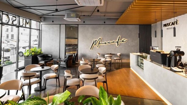 Ein modernes Café-Interieur mit runden Tischen und Stühlen, einer Theke und einem großen Fenster mit Blick auf die Straße.