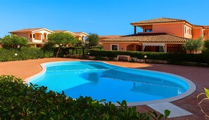A swimming pool surrounded by a landscaped garden, with a large house in the background. - Apartment 'Casa Vacanze Gelso' with Shared Pool, Private Garden and Air Conditioning (Murta Maria)