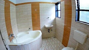 A bathroom with a bathtub, sink, toilet, and a window. - KDM Hotel Sai Geeta (Shirdi)