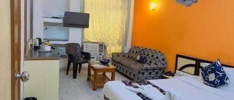 Quarto de hotel com cama, sofá, escrivaninha com computador e ventoinha no teto.