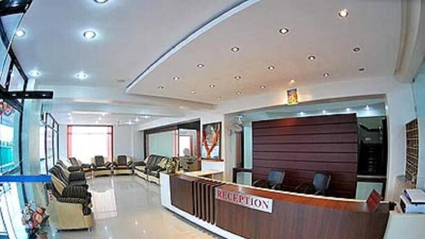 A reception area with a wooden reception desk, several sofas, and a glass partition. - KDM Hotel Sai Geeta (Shirdi)