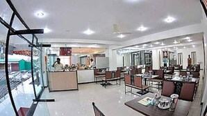 A modern restaurant with a central counter and multiple dining tables. - KDM Hotel Sai Geeta (Shirdi)