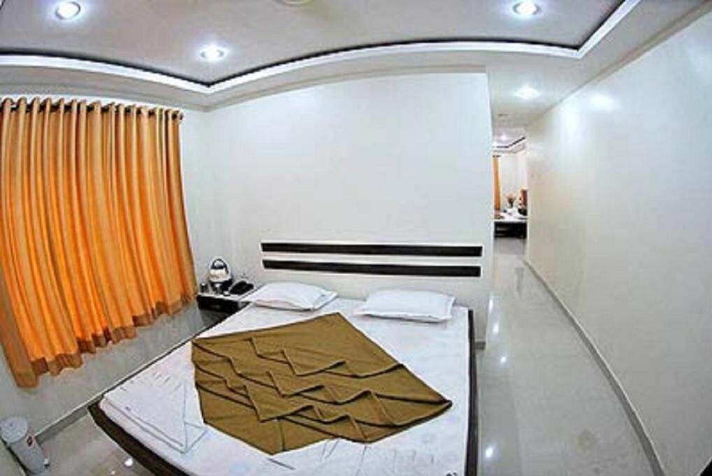 A hotel room with a bed, a nightstand, a mirror, and a window with curtains.