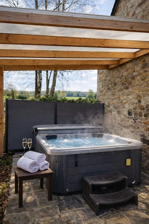 A hot tub under a wooden pergola with stone walls, two glasses of wine, and towels on a table. - Le refuge de Séve: estate with games room and jacuzzi, ideal for families (Momignies)
