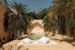 A pool area with a sofa and pillows, surrounded by palm trees and a stone wall. - Serene Luxury 2BR Private Pool Villa - Canggu (Bali)