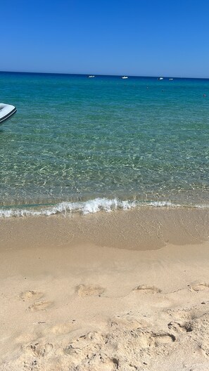Una playa con agua turquesa cristalina, una orilla de arena y varios barcos a lo lejos.
