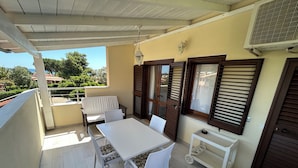 Un balcon avec une table et des chaises, une petite table avec un plateau, et un climatiseur fixé au mur.