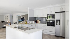 A modern kitchen with white cabinetry, stainless steel appliances, and a central island with a sink. - Serenity - A place for relaxing (Corlette)