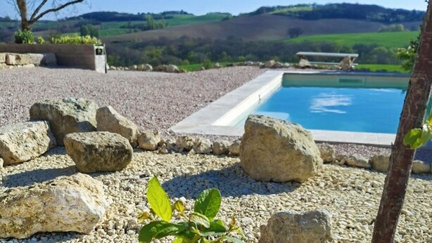 Une piscine avec vue sur les collines, entourée de rochers et d’un arbre.