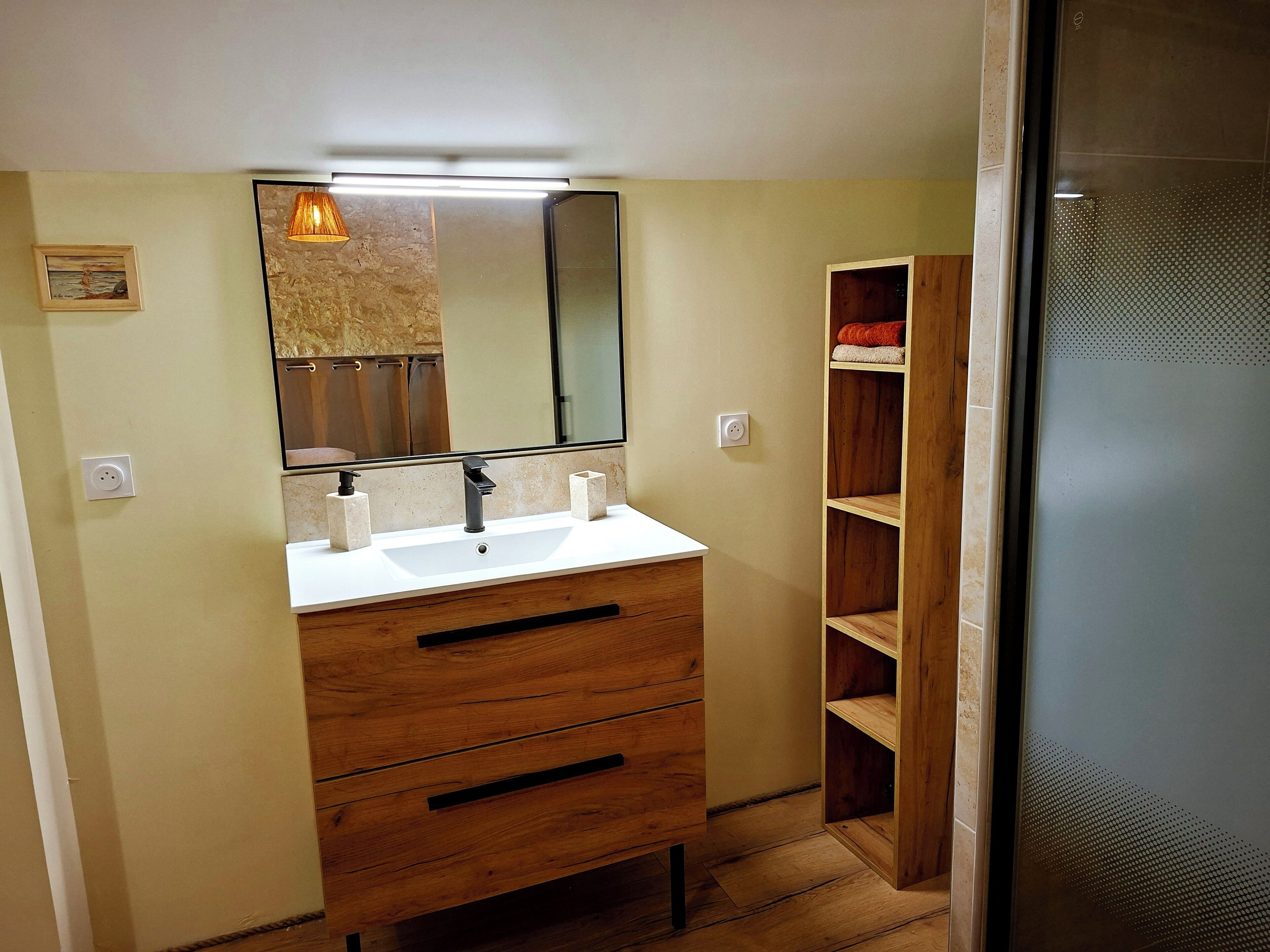 A bathroom with a wooden vanity, a mirror, and a shelf unit.