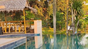 A poolside setting with a clear pool, a thatched-roof structure, and a table with fruit and a drink. - Tom Star Pool Villa Layan 3BR Large pool, mountain view for the rooftop (ตำบล ศรีสุนทร)