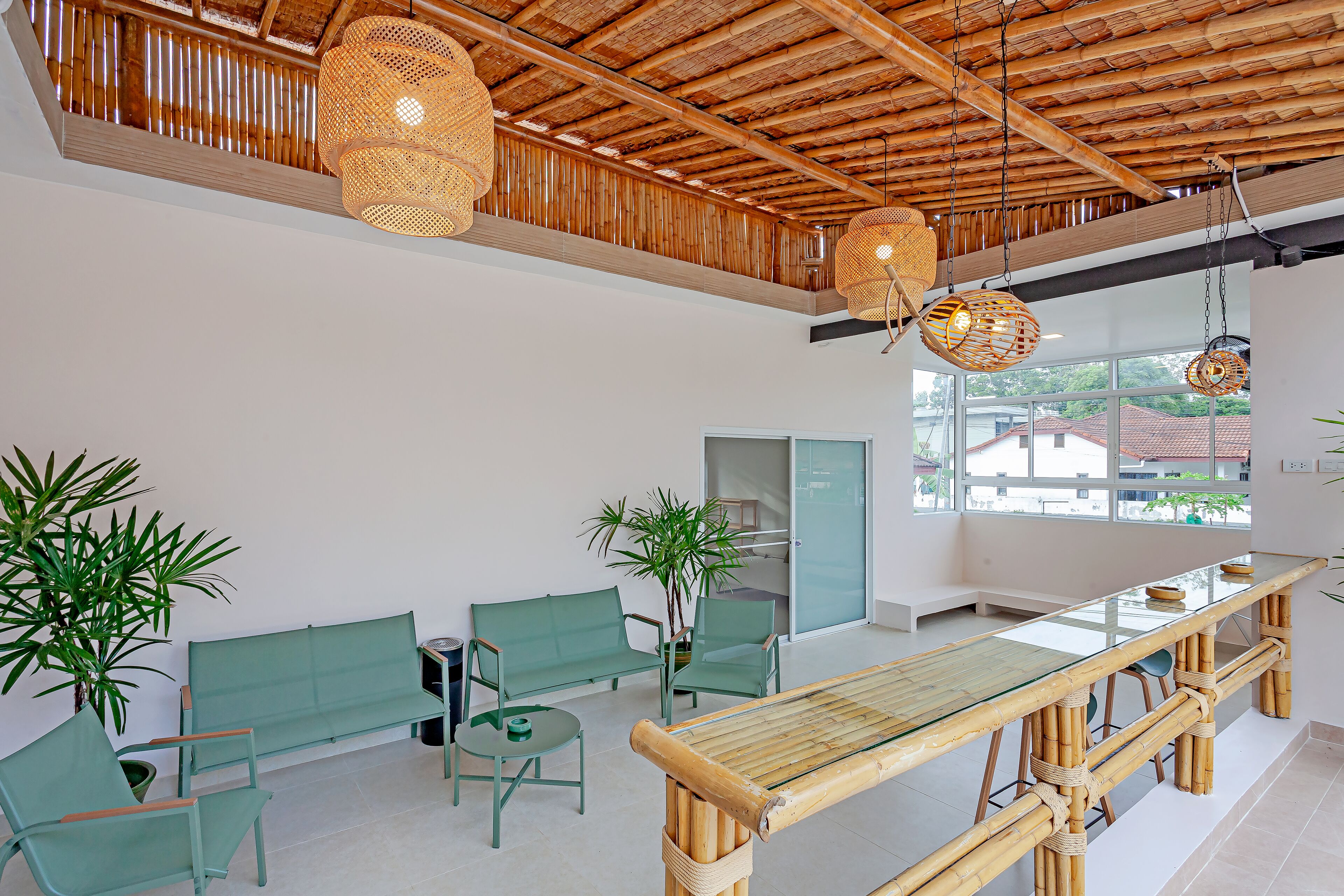 Eine großzügige Lobby mit hoher Decke, grünen Sitzgelegenheiten, einem Bambustisch und großen Fenstern mit Blick ins Freie.