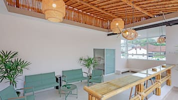 Eine großzügige Lobby mit hoher Decke, grünen Sitzgelegenheiten, einem Bambustisch und großen Fenstern mit Blick ins Freie.