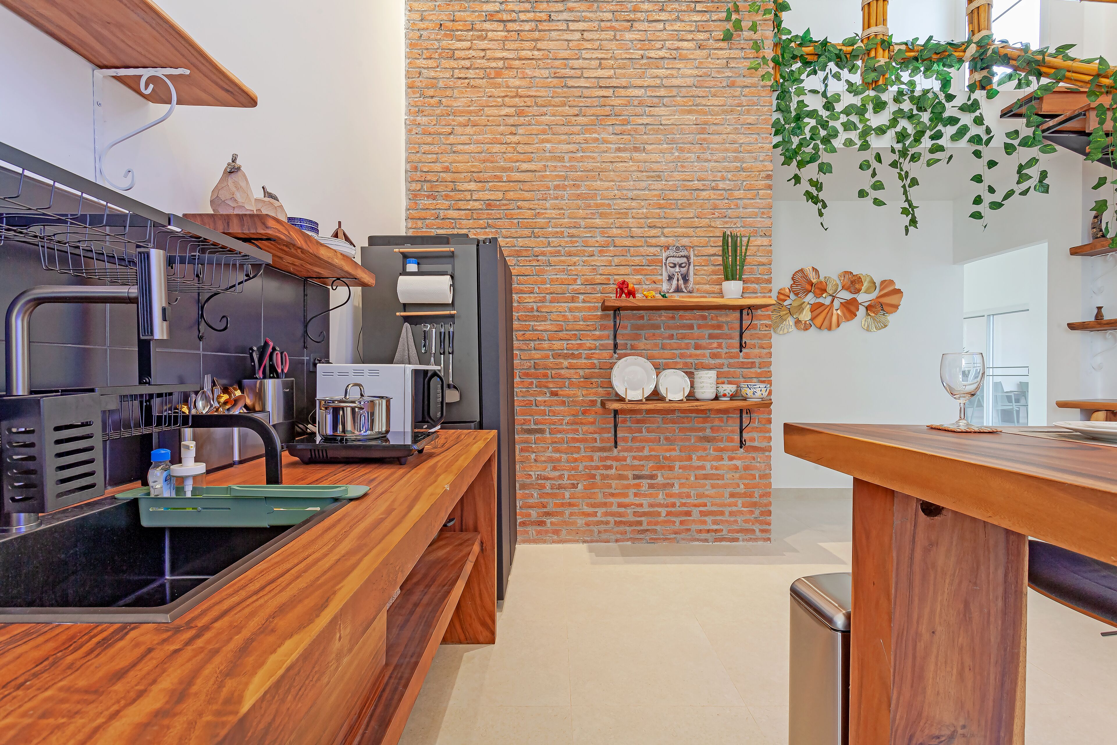A modern kitchen with a brick wall, wooden shelves, and a black countertop.