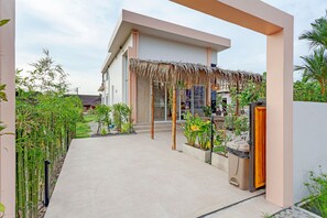 Ein modernes Gebäude mit überdachter Einfahrt, einem Betonweg und verschiedenen Pflanzen.