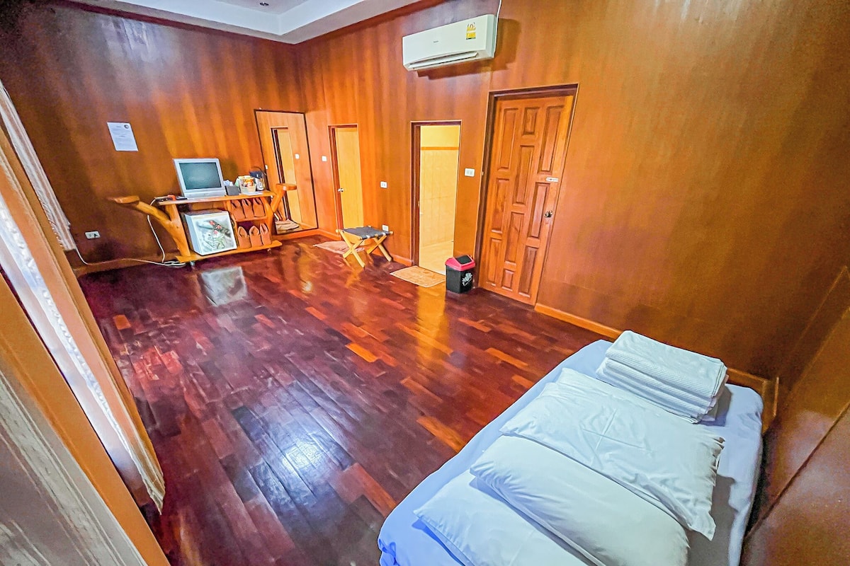 A room with wooden flooring, a bed, a desk with a computer, and two doors.