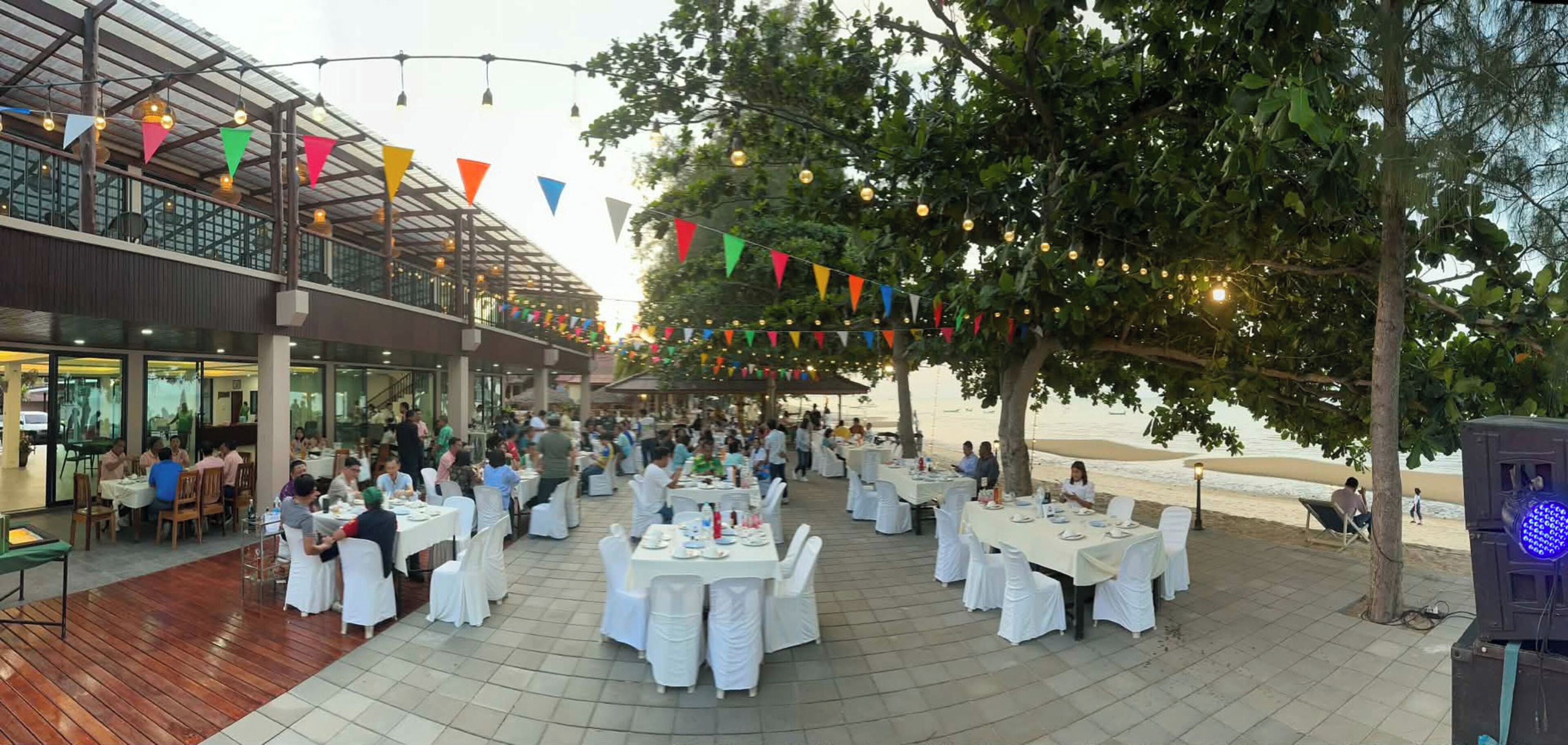 An outdoor dining area with tables and chairs, a covered seating area, and a view of the beach.