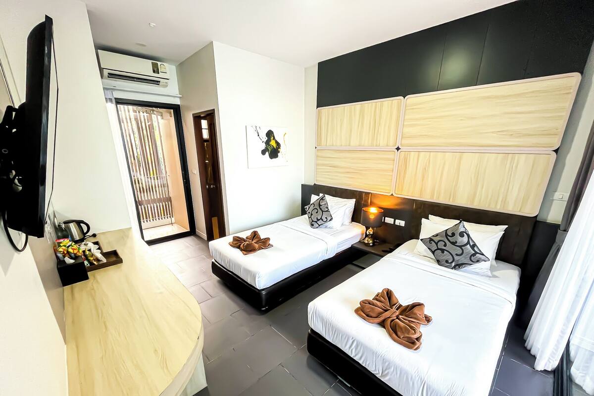 A hotel room with two beds, a desk, a TV, and a window with blinds.