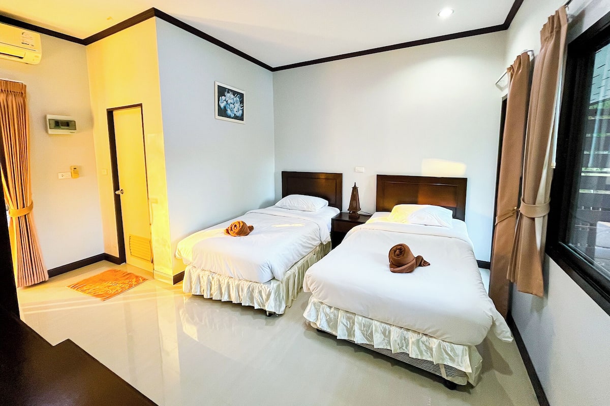 A hotel room with two beds, a bedside table, a nightstand, a window with curtains, and a door.