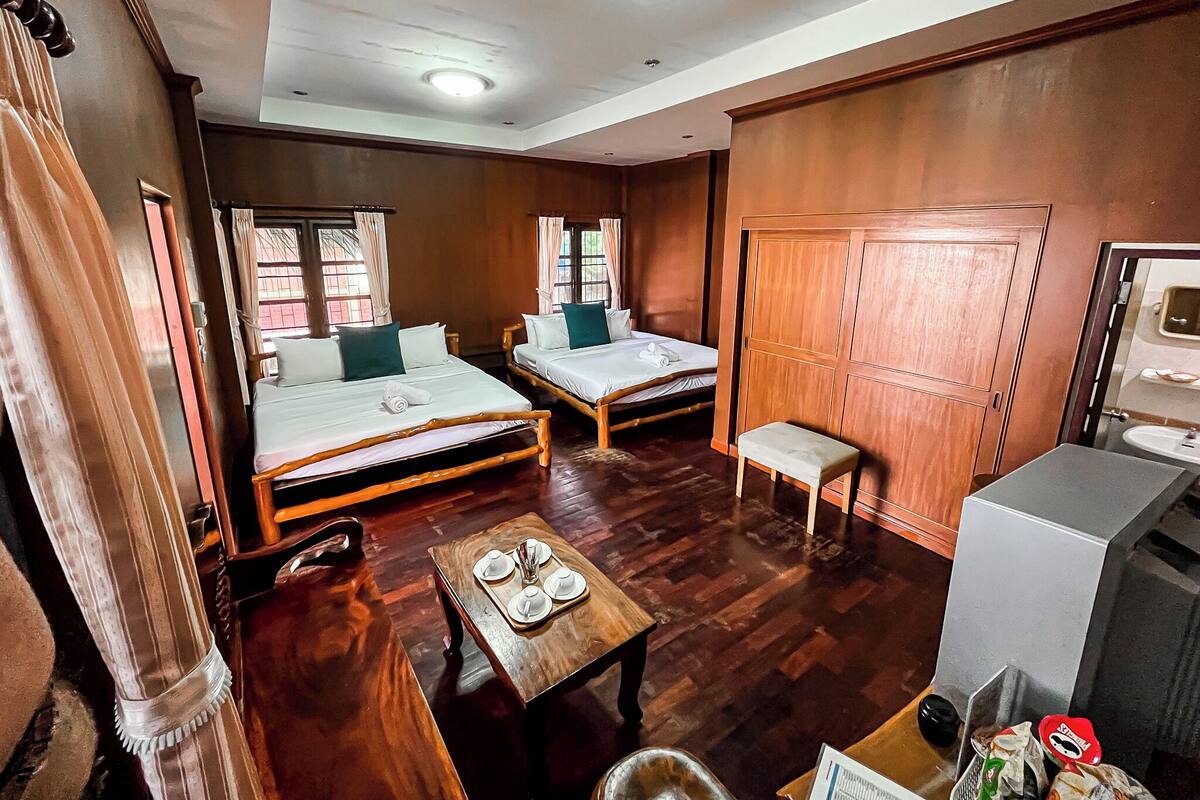 A hotel room with two beds, a small table with a tray, a wooden wardrobe, and a bathroom with a sink.