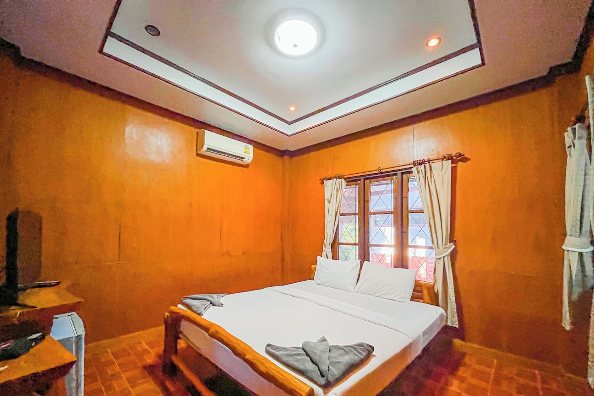 A hotel room with a bed, an air conditioning unit, a window with curtains, and a wooden floor.