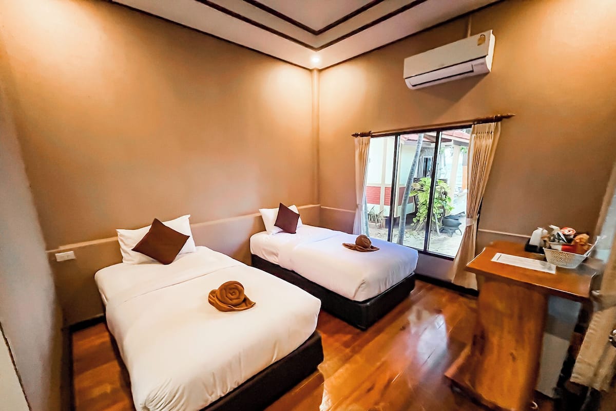 A hotel room with two beds, a wooden floor, a small desk, and an air conditioning unit.