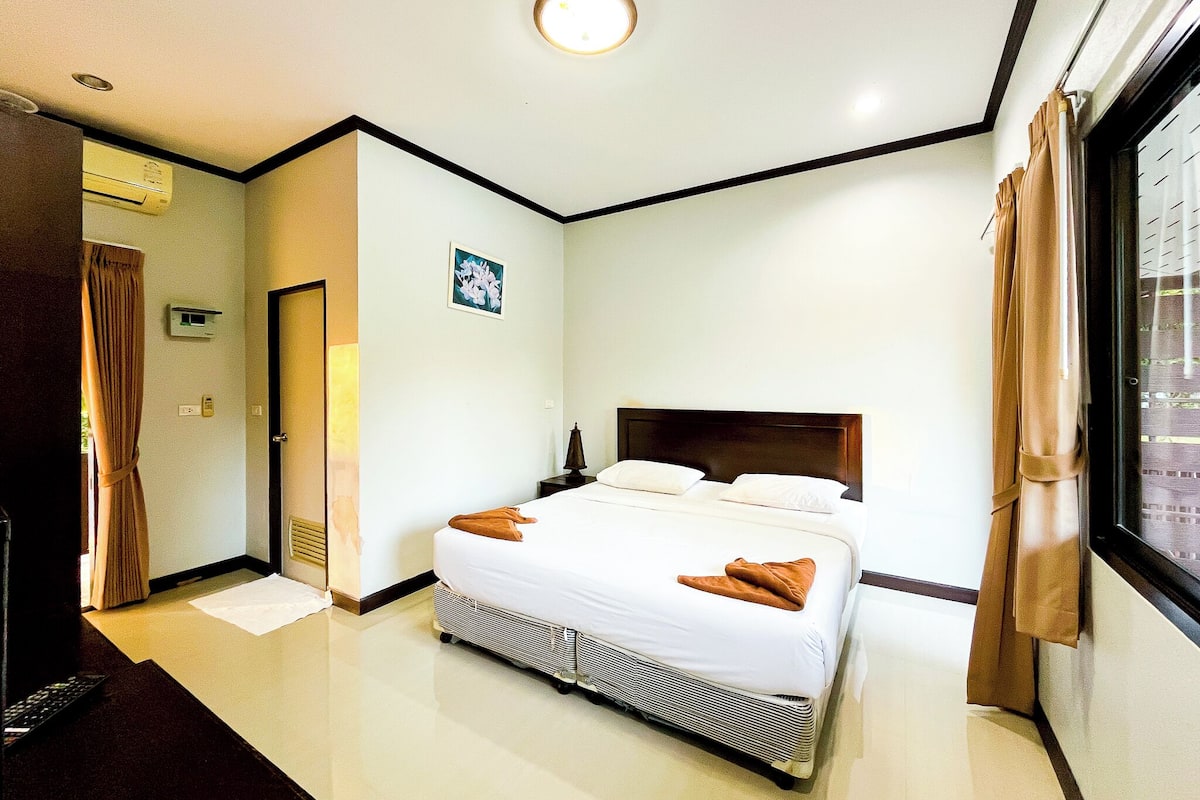 A hotel room with a bed, a nightstand, a window with curtains, and a door.