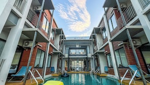 Un hotel moderno con una piscina central, varios balcones y cielo despejado.