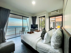 A modern hotel room with a large bed, a TV, and a balcony with a view of the sea. - Leamsai Beach Resort (Chaiya)