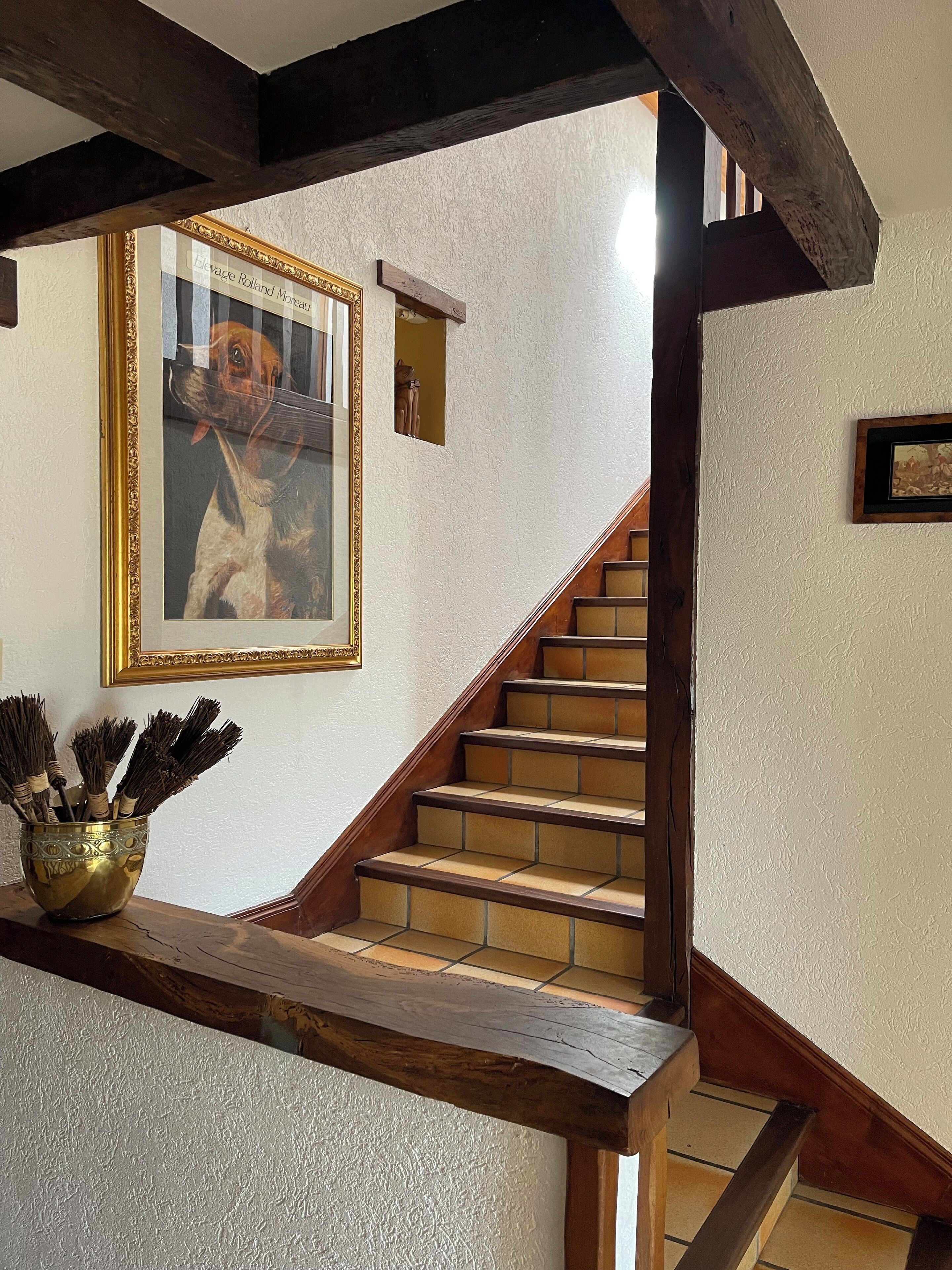 A staircase with wooden steps and a wooden handrail, leading to a landing with a framed picture and a brass bowl with twigs.