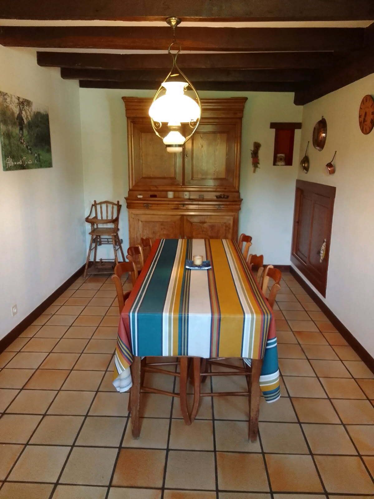 A dining room with a large wooden table, chairs, and a hanging light fixture.