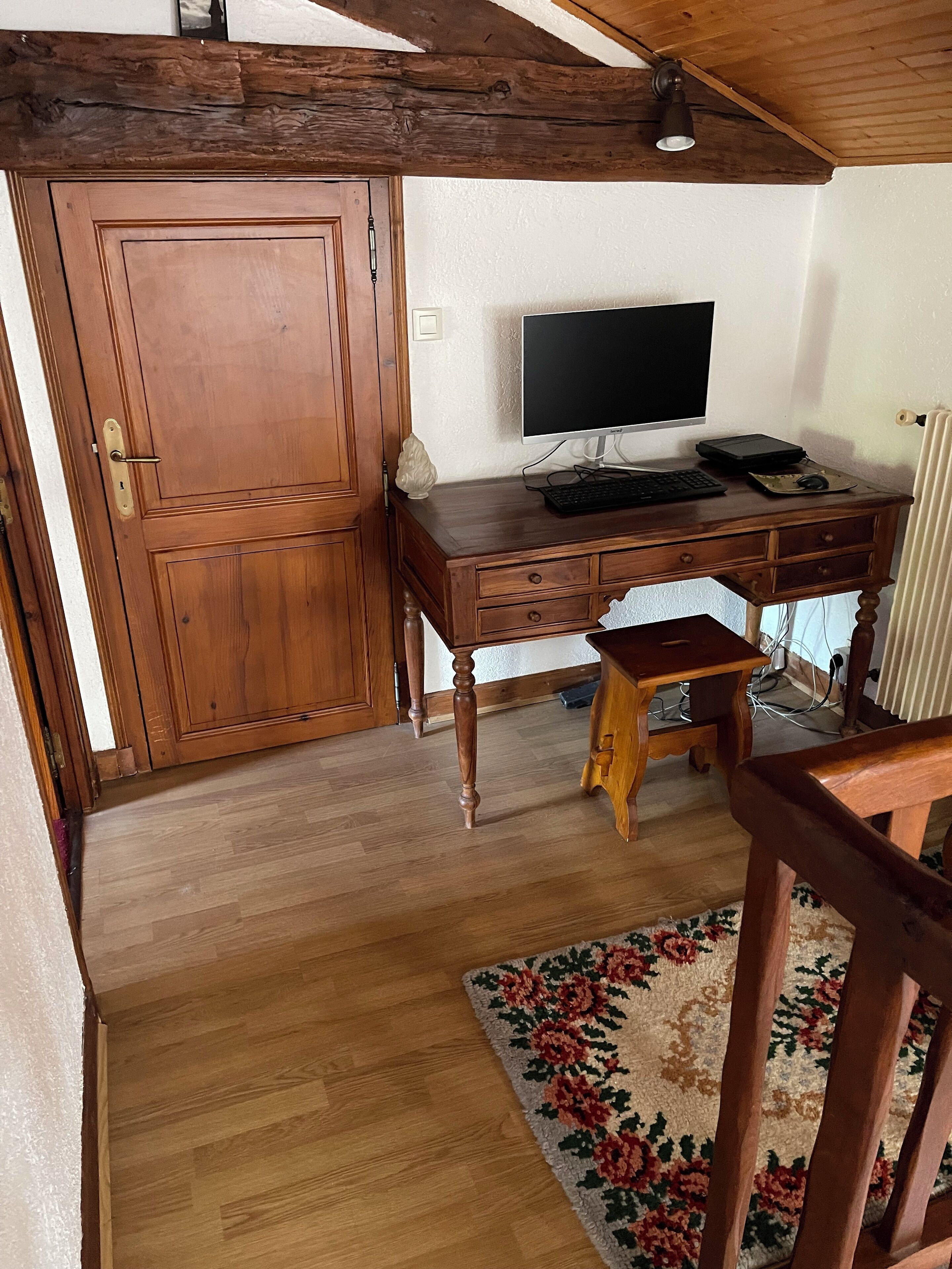 Ein Holztisch mit einem Computer, einer Tastatur und einer Maus. Vor dem Tisch steht ein hölzerner Stuhl.
