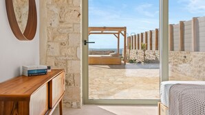A room with a wooden desk, a mirror, and a bed. There is a door leading to an outdoor area with a stone wall and a wooden pergola. - Serene Villas - Villa Thalassini by Estia (Minoa Pediada)