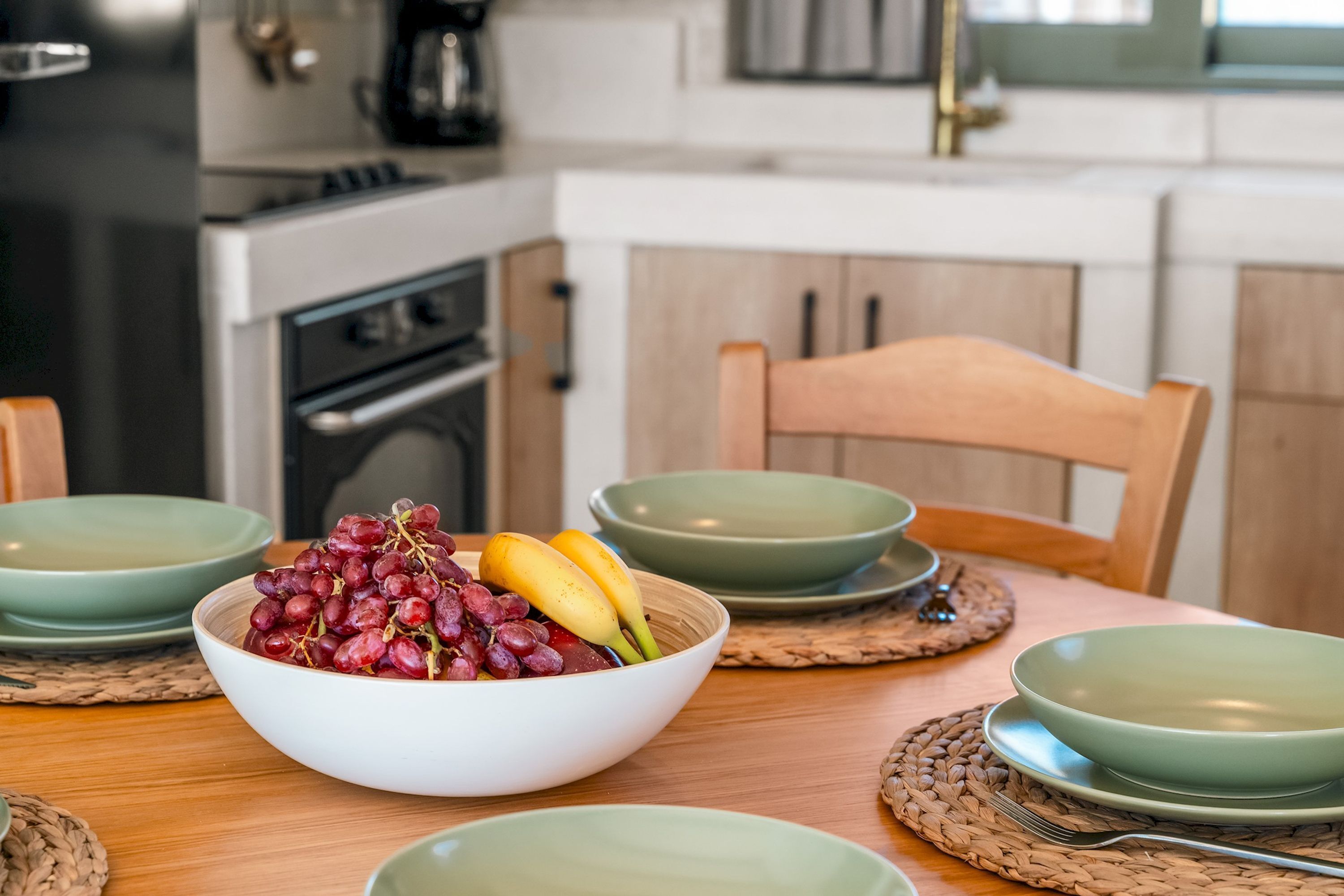 A dining table with a bowl of fruit, green plates, and woven placemats.