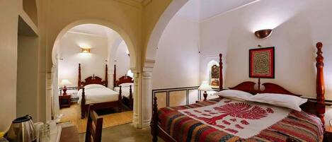 Ein Hotelzimmer mit einem großen Bett, einem Holztisch und einem Stuhl. An der Decke hängt ein Ventilator und an der Wand befindet sich ein gerahmtes Bild.