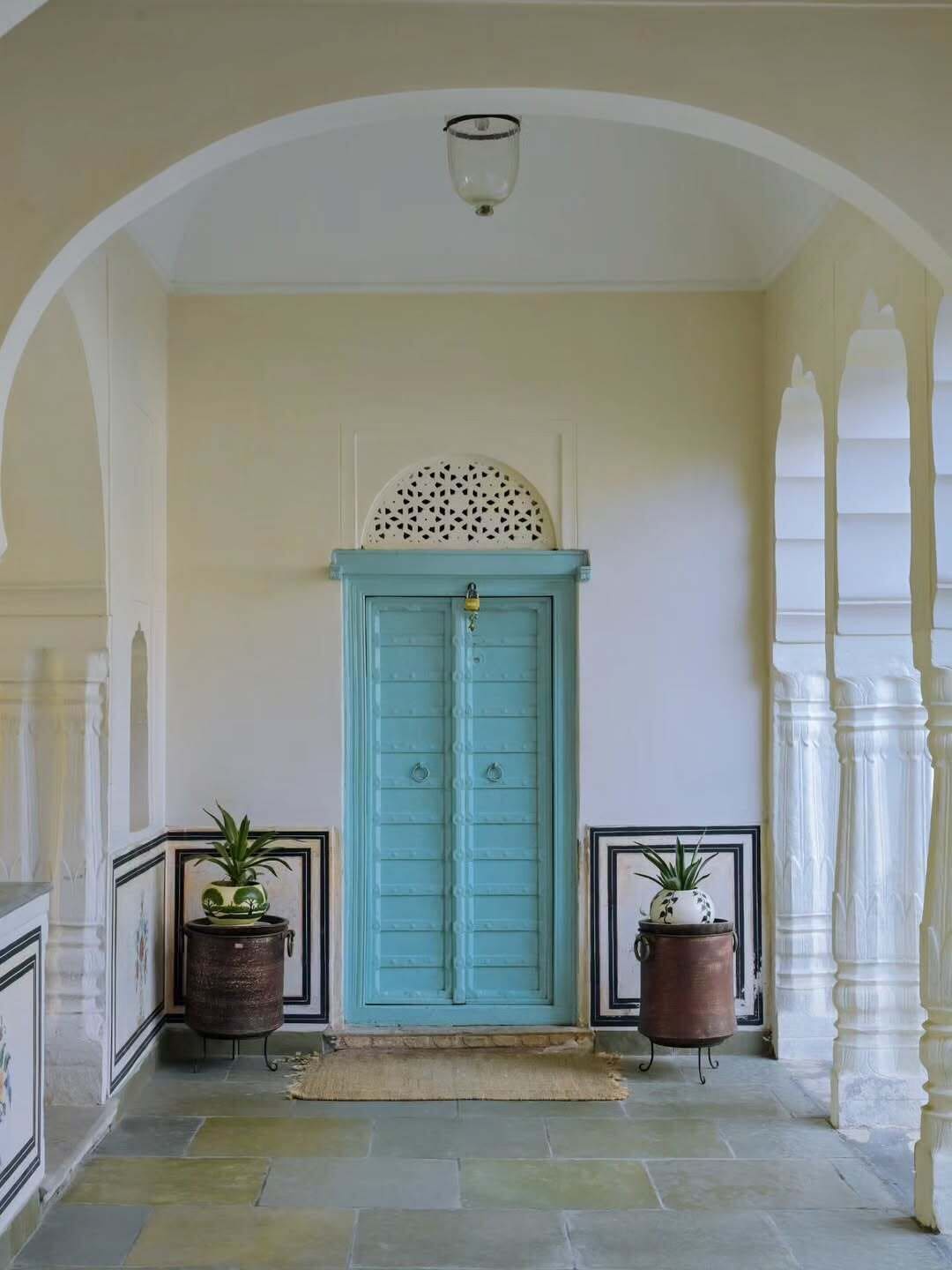 A hallway with a turquoise door, white columns, and two potted plants.
