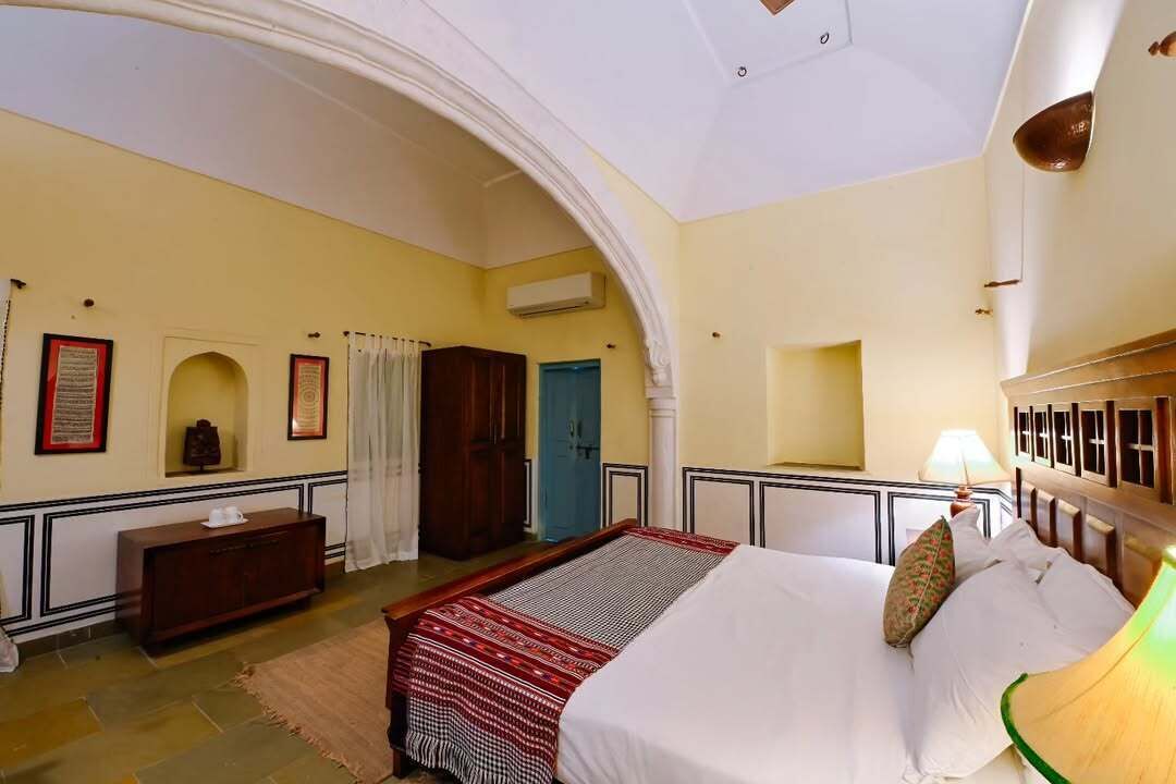 A room with a bed, a wooden cabinet, a mirror, and a door.