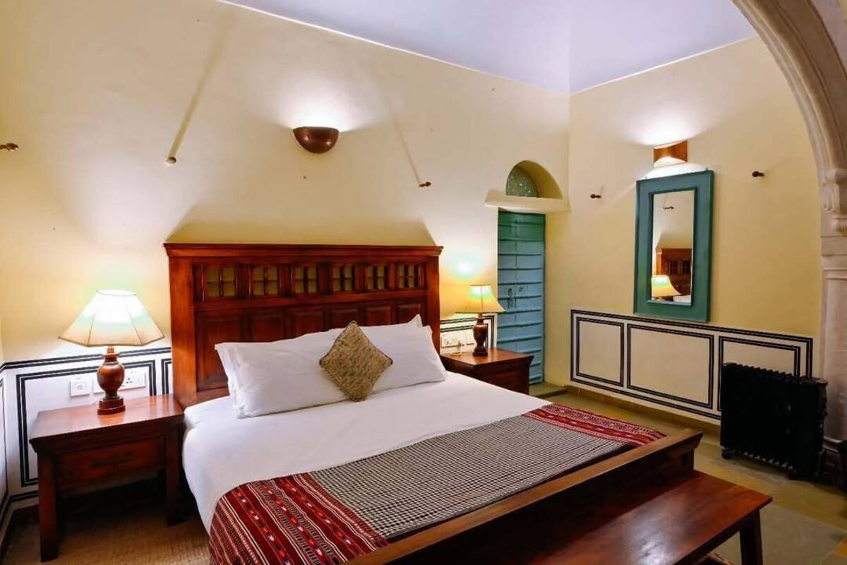 Ein Hotelzimmer mit einem großen Bett, zwei Nachttischen mit Lampen, einem hölzernen Kopfteil, einem Spiegel und einer Tür mit grünem Rahmen.