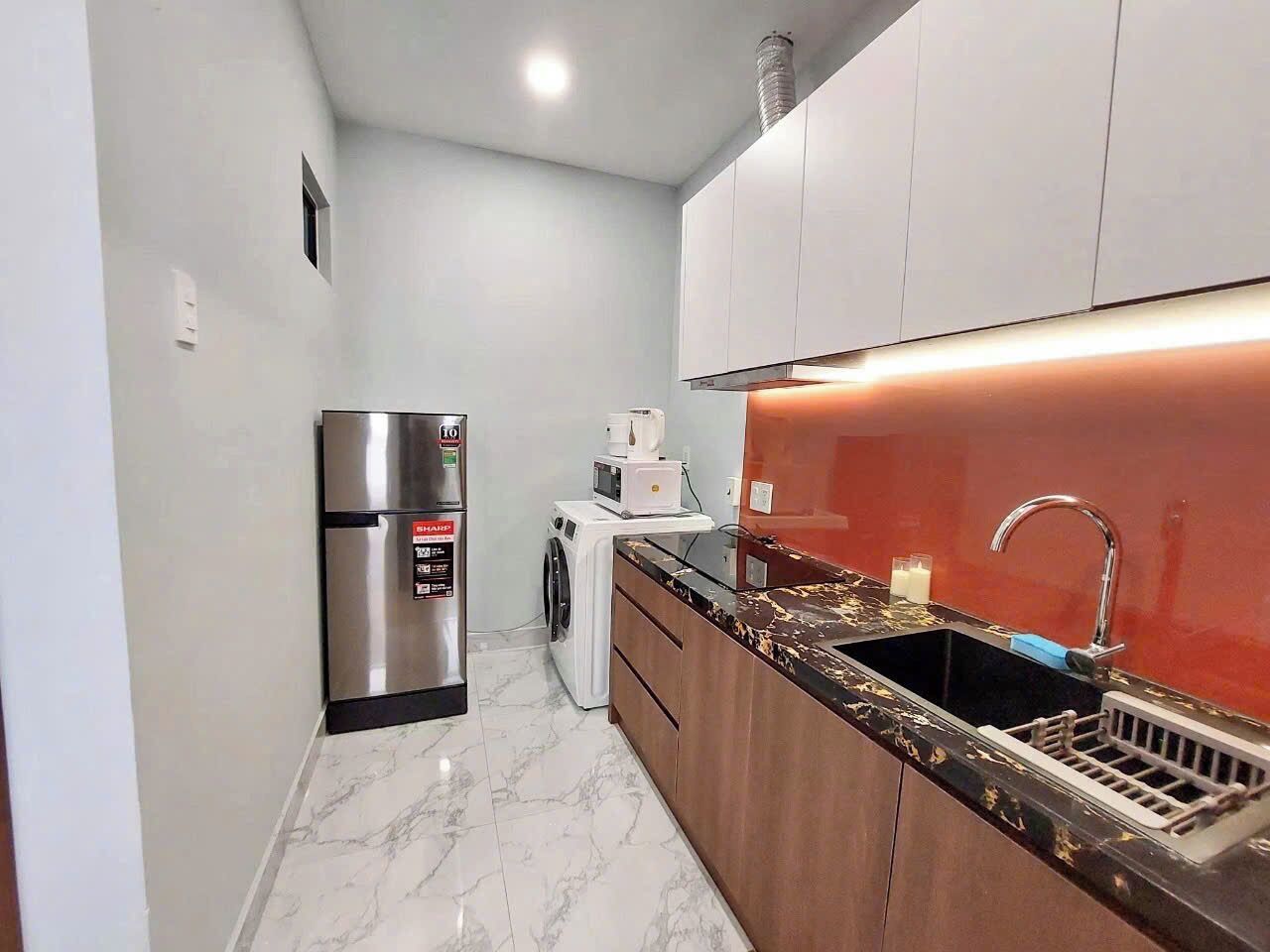 A compact kitchen with a stainless steel refrigerator, a washing machine, and a sink with a modern faucet.